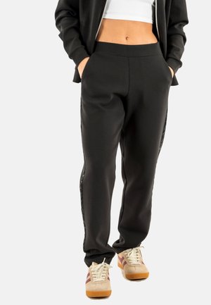 Pantalones sudadera negros con una cintura elástica y bolsillos laterales, que presentan un panel de acento texturizado y se combinan con zapatillas beige.