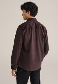 Camicia marrone con bottone, dotata di un motivo testurizzato, maniche lunghe e orlo dritto. Presenta un colletto classico e polsini with bottoni.