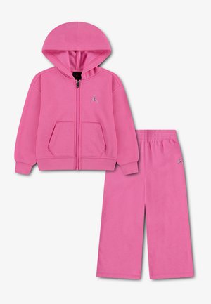 Różowy dres z bluzą z kapturem zapinaną na zamek i dopasowanymi spodniami, oba z małym srebrnym logo Jumpman, przedstawione na jednolitym tle.