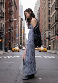 Vzdušné sivé maxišaty s kvetinovým vzorom, bočným rozparkom, v kombinácii s čiernou koženou bundou a čiernymi podpätkovými čižmami. Mesto v pozadí.