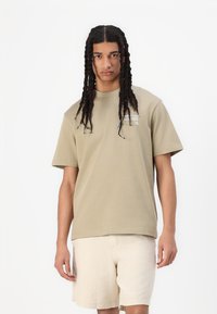 T-shirt verde oliva realizzata in morbido cotone, con scollatura rotonda e maniche corte, caratterizzata da una stampa grafica sottile sulla parte frontale.