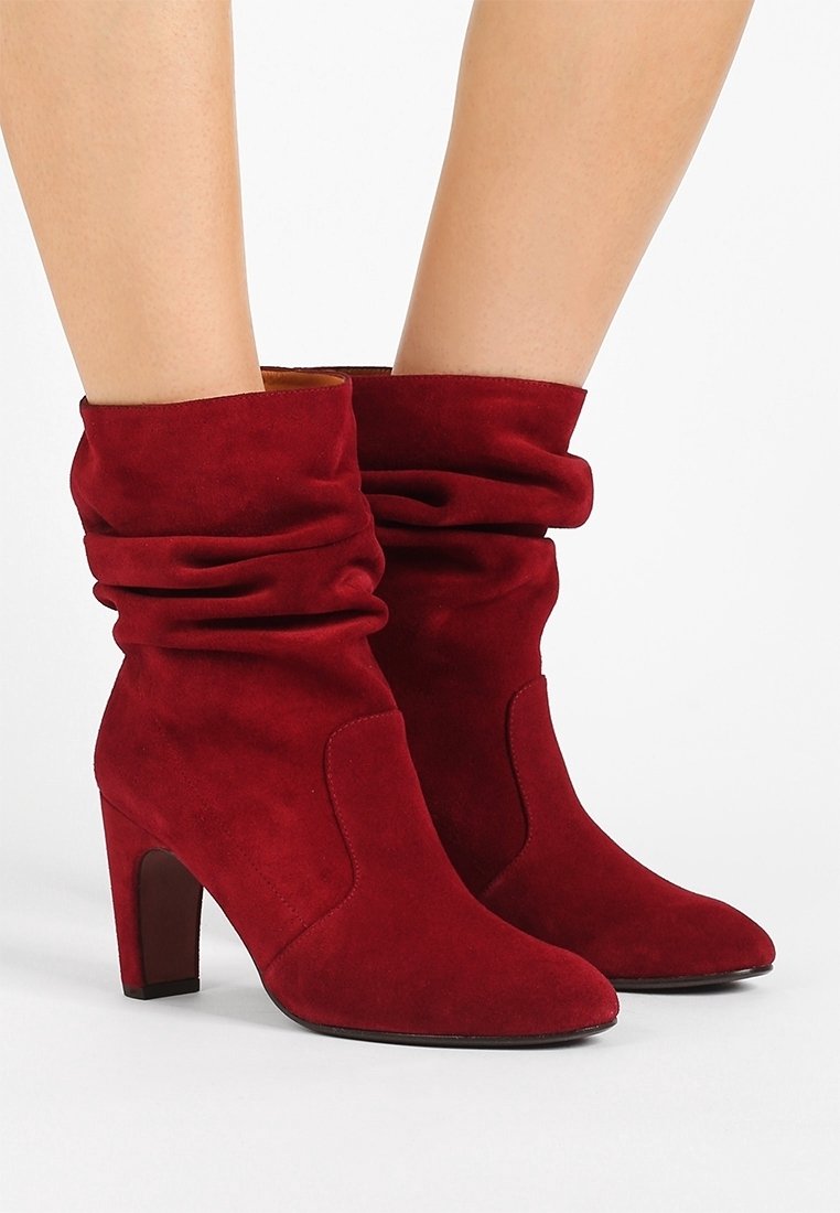 Botas de tobillo de ante rojo con parte superior arrugada, punta afilada y tacón de 10 cm. Textura suave con costuras mínimas.