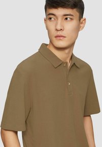 Polohemd in olivgrün, kurzärmlig, strukturierter Stoff, mit einer Dreiknopf-Leiste in hellbraunen Knöpfen, klassisches Kragen-Design.