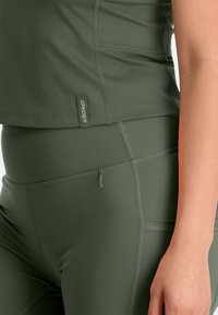 Olijfgroen sporttop en leggings, met platte naden, een logo-tag en een gladde textuur. Het ontwerp heeft een strakke silhouette.