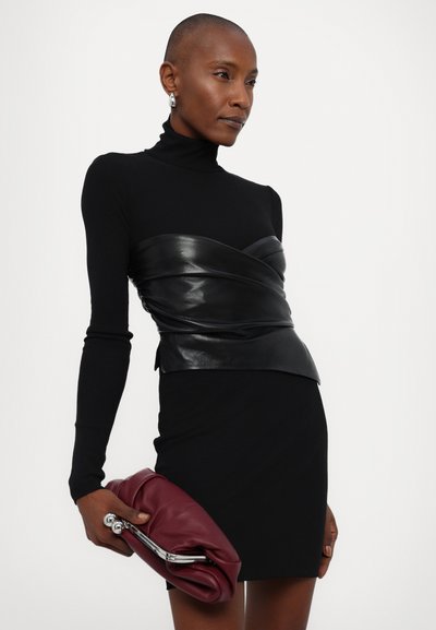 Haut noir à manches longues avec un overlay en cuir ajusté à la taille, associé à une mini jupe noire. Tient une pochette bordeaux avec quincaillerie argentée.