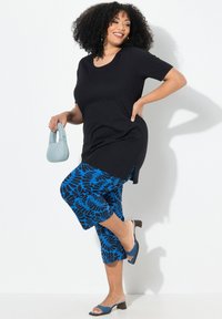 Haut noir à manches courtes associé à un pantalon capri bleu à motifs et des sandales à talons bleues à enfiler. Le mannequin tient un sac à main bleu clair.