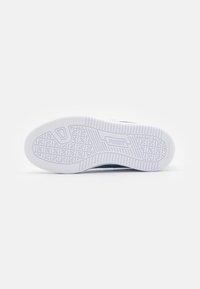 Suela de zapatilla de goma blanca con patrón de agarre texturizado; presenta una forma redondeada y un talón levantado; con la marca "PUMA" en el lateral.