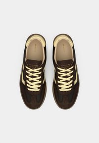 Καφέ αθλητικά παπούτσια με συνδυασμό σουέτ και διχτυωτού υφάσματος, με κίτρινες κορδόνια και λεπτομέρειες, στρογγυλεμένη μύτη και ανάγλυφη σόλα.