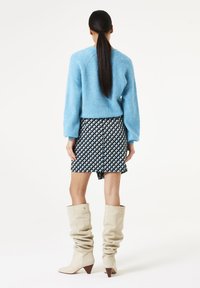 Lichtblauwe trui met raglanmouwen, gecombineerd met een zwart-wit gestippelde mini-rok. Beige kniehoge slouchlaarzen accentueren de outfit.