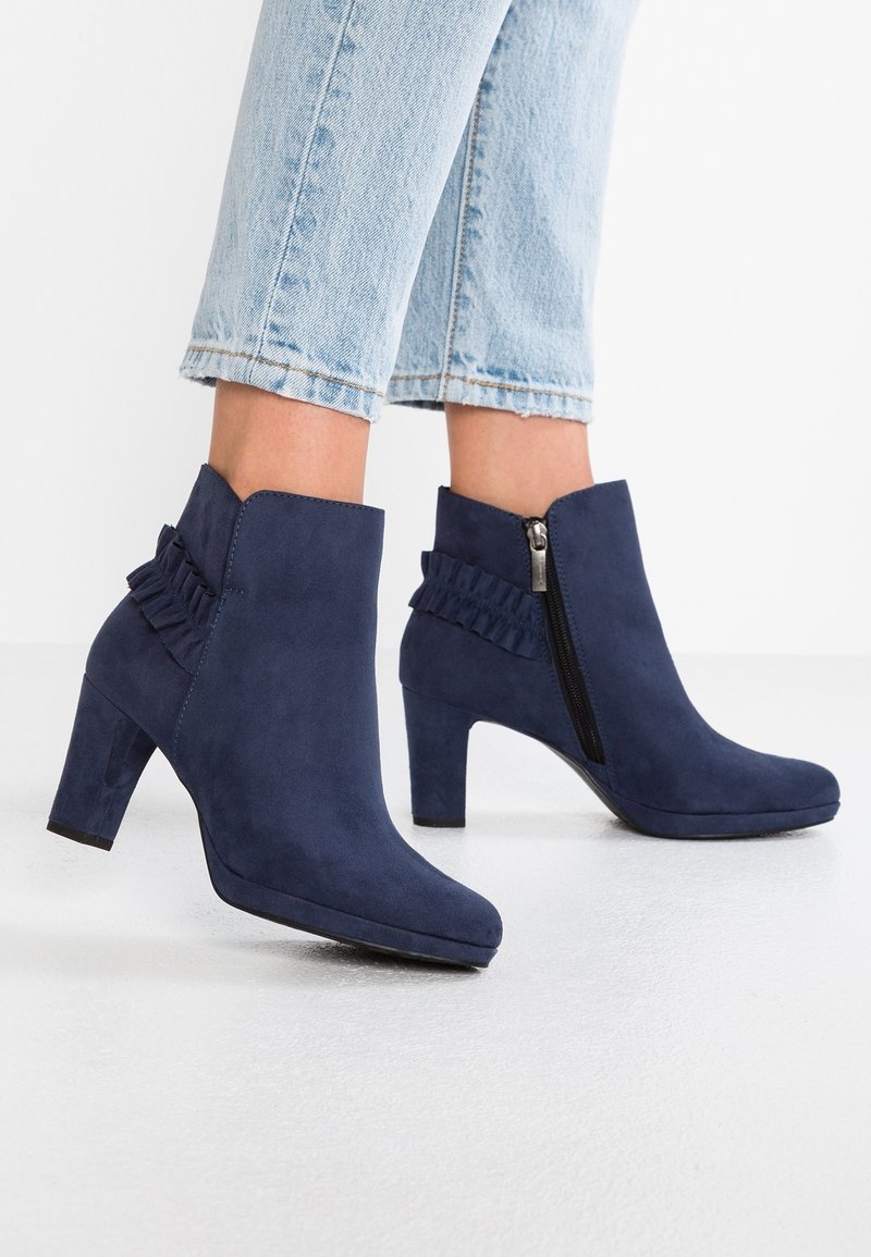 Bottines en daim bleu marine avec fermeture éclair latérale et détail volanté, portées avec un jean court bleu clair.
