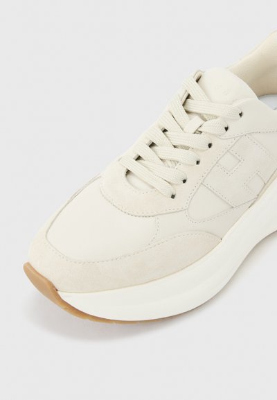 Αθλητικό παπούτσι κρεμ χρώματος με χοντρή λευκή σόλα, υφή σουέντ και λείες δερμάτινες όψεις, λευκά κορδόνια και διακριτικό ανάγλυφο λογότυπο στο πλάι.