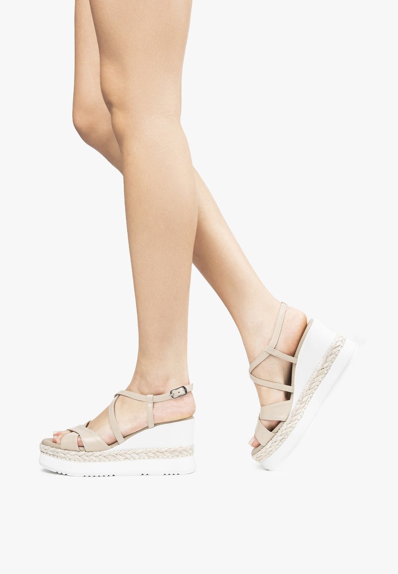 Beige kilehæle sandaler med et vævet jute-detalje, justerbar ankelrem og gummisål. Designet med flere krydsede remme på overdelen.
