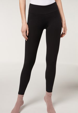Leggings neri realizzati in tessuto elasticizzato, con una vita alta e una texture liscia, abbinati a calzini leggeri rosa chiaro.