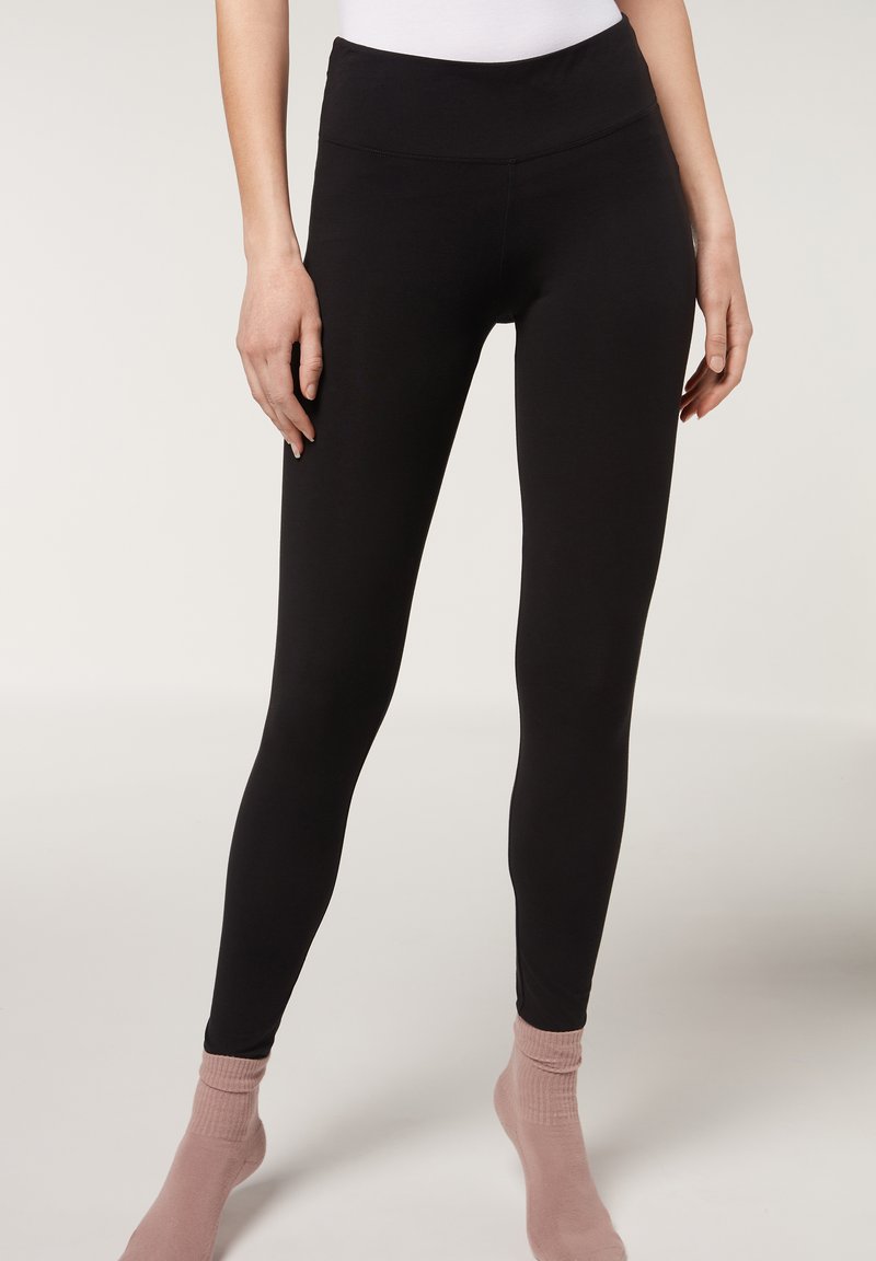 Leggings neri realizzati in tessuto elasticizzato, con una vita alta e una texture liscia, abbinati a calzini leggeri rosa chiaro.