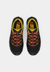 Černé sportovní boty s texturovaným povrchem, které mají živé oranžové a žluté šňůrky a polstrovaný žlutý vnitřek.