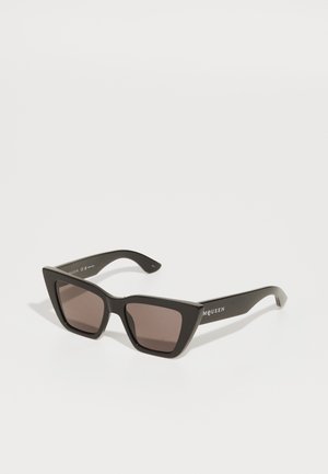 Schwarze übergroße Sonnenbrille mit geometrischer Katzenaugenform, dunkeltönenden Gläsern und ohne sichtbare Beschlagdetails.
