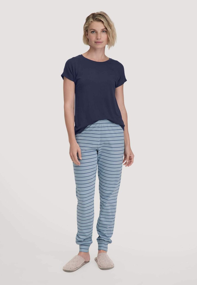 Marineblaues T-Shirt mit kurzen Ärmeln, kombiniert mit hellblauen gestreiften Schlafanzughosen. Die Hausschuhe haben eine weiche Textur in neutraler Farbe.