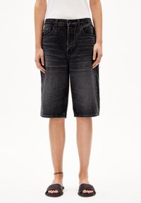 Donkergrijze denim bermuda shorts met een relaxed fit, voorzien van zakken, riemlussen en een ruwe zoom. Draagt met zwarte slippers.