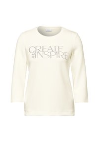 Cream long-sleeve shirt with a round neckline, featuring "CREATE INSPIRE" in sparkly lettering on the front. Smooth fabric texture.