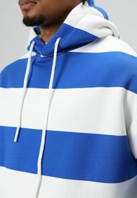 Blauw-wit gestreepte hoodie gemaakt van zachte stof, met een capuchon met trekkoord en opvallende horizontale strepen over de borst.