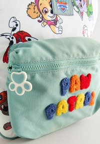 Sac à dos avec un design ludique inspiré de Paw Patrol, comportant des chiens en cartoon. Corps principal en blanc, poche avant en vert menthe avec des lettres colorées et texturées.