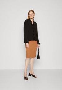 Black long-sleeve top with ruffles, paired with a ribbed brown pencil skirt. Finished with black block-heeled sandals and a small handbag.