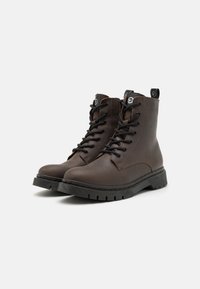 Botas de cuero marrón con cordones y puntera redonda, suela de goma negra resistente y costuras en contraste. Cuenta con una tira en la parte posterior para facilitar el calzado.