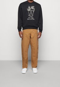 Sudadera negra con diseño de arte lineal en blanco y texto, combinada con pantalones beige de corte holgado que cuentan con bolsillos y costuras sutiles. Zapatillas blancas.
