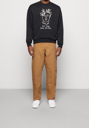 Sudadera negra con diseño de arte lineal en blanco y texto, combinada con pantalones beige de corte holgado que cuentan con bolsillos y costuras sutiles. Zapatillas blancas.