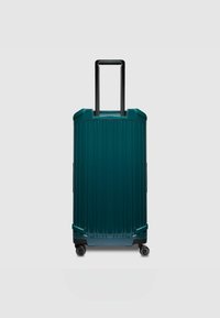 Teal koffer met harde schaal en verticale ribbels, zwarte inklapbare handgreep en vier wielen voor mobiliteit, met een strak en duurzaam ontwerp.