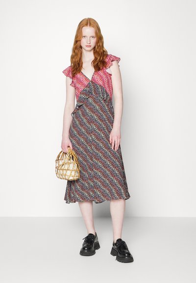 Vestido floral com mangas com volantes, apresentando um corpete estampado em rosa e uma saia preta fluida. Modelo segura uma bolsa de palha. Sapatos pretos.