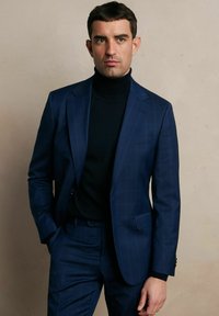 Granatowy garnitur o dopasowanym kroju z subtelnym wzorem w kratkę, połączony z czarnym golfem. Posiada ostre klapy i przednie kieszenie.