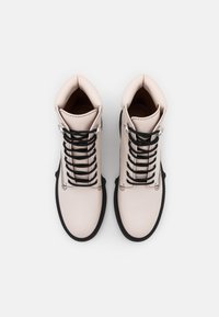 Bottes en cuir rose clair avec lacets noirs, bout rond, œillets argentés et semelle noire texturée. Finition lisse, design hauteur cheville.