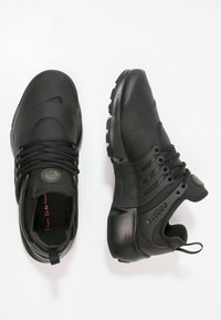 Černé sportovní boty s texturovaným koženým svrškem, kulatou špičkou a silnou gumovou podrážkou. Vybavení zahrnuje šňůrky a akcent s logem na jazyku.
