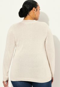 Helle beige Strickpullover mit langen Ärmeln, rundem Ausschnitt und geripptem Saum, kombiniert mit engen dunkelblauen Jeans.