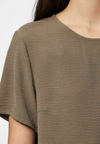 Top marrone a maniche corte con scollatura a girocollo, realizzato in un tessuto testurizzato e con una leggera lucentezza, privo di cuciture visibili o decorazioni.