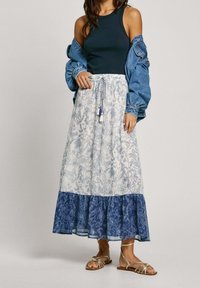 Lång blommig kjol i vitt och blått, med ett texturerat mönster och en fläktkant i lager vid fållen. Kombinerad med en mörk linne och en jeansjacka.