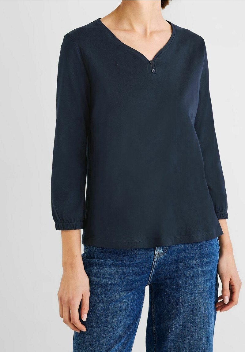 Mörkblå långärmad topp med V-ringning och en enda knappknäppning, med elastiska manschetter och en avslappnad passform, tillverkad av ett slätt tyg.