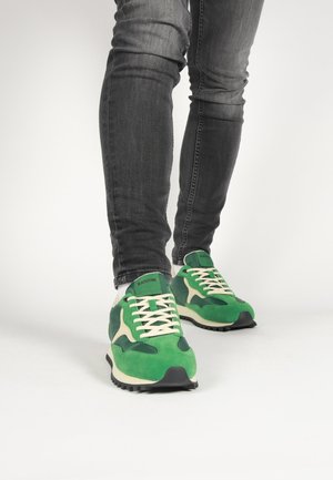 Grüne und cremefarbene Sportsneaker aus Wildleder und synthetischen Materialien, mit einem weißen Schnürdesign und einer schwarzen Gummisohle.