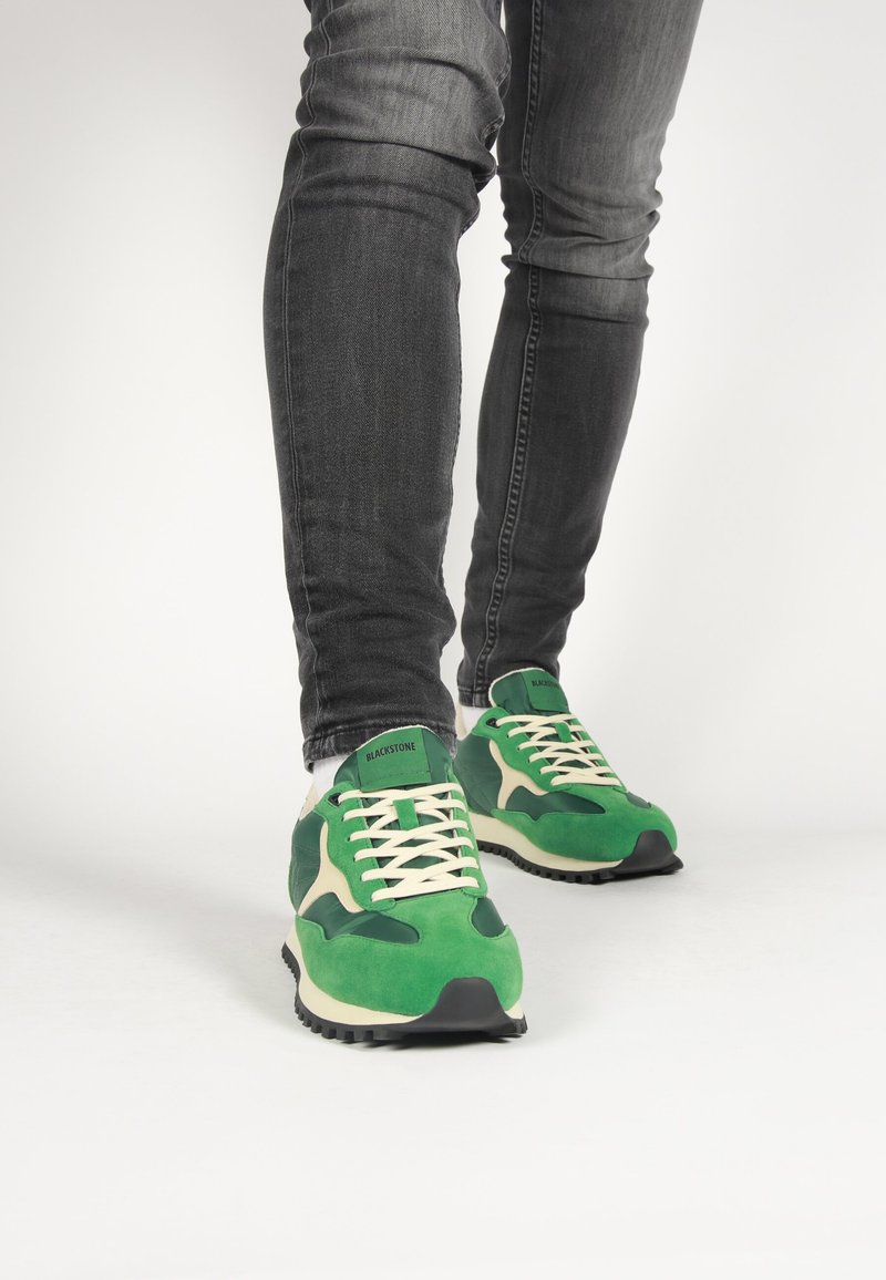 Zelené a krémové atletické tenisky z semišu a syntetických materiálov, s bielym šnurovaním a čiernou gumovou podrážkou.