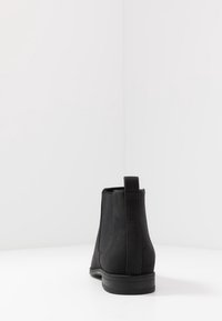 Botas Chelsea de ante negro con paneles laterales elásticos, una lengüeta en la parte posterior y una suela de goma texturizada. Acabado suave, diseño de altura hasta el tobillo.