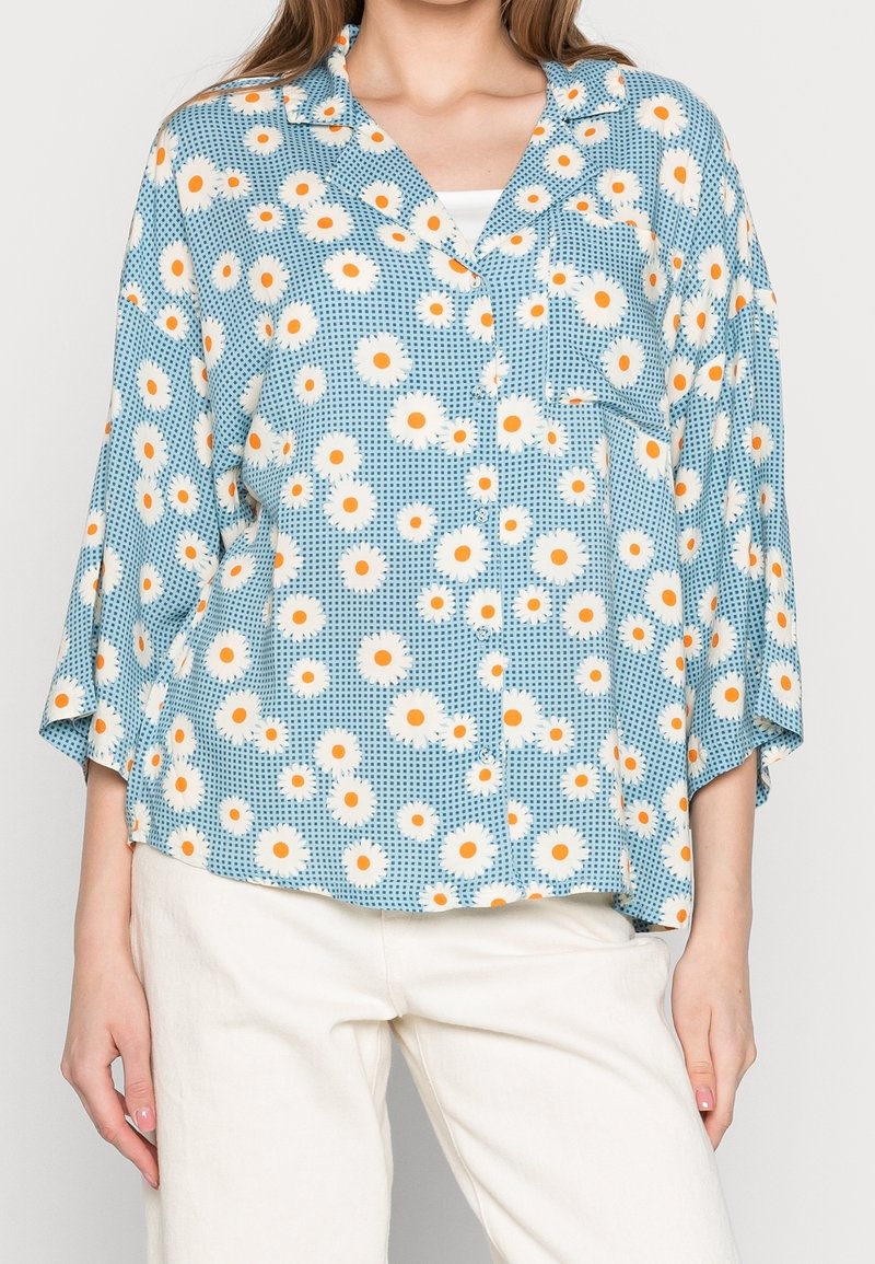 Blusa leggera a maniche corte in tessuto blu con un motivo floreale bianco e arancione, con chiusura frontale a bottoni e tasca applicata.
