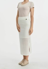 Biała dziana spódnica midi o fakturowanym wzorze, z bocznym rozcięciem i elastycznym pasem. W połączeniu z beżową dopasowaną koszulą i neutralnymi trampkami.