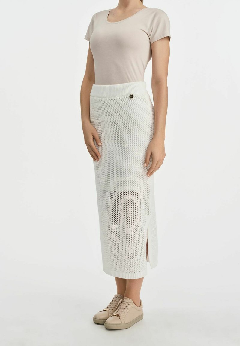 Biała dziana spódnica midi o fakturowanym wzorze, z bocznym rozcięciem i elastycznym pasem. W połączeniu z beżową dopasowaną koszulą i neutralnymi trampkami.