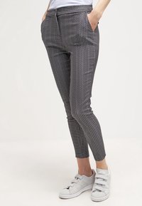 Ben iförda svarta och vita mönstrade slim jeans med händerna i fickorna, kombinerat med vita sneakers med kardborreband.