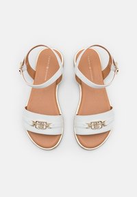 Białe skórzane płaskie sandały na ramiączkach, ze złotym łańcuchowym detalem na przednich ramiączkach oraz brązowymi wyściełanymi wkładkami, marki Tommy Hilfiger.