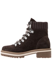 Brązowy zamszowy botek za kostkę z prążkowanym wykończeniem, metalowymi oczkami i sznurowanym przodem. Oferuje solidną gumową podeszwę z lekkim obcasem.