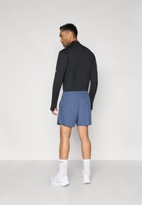 Herreantrekk med en svart langermet skjorte og lyseblå shorts. Shortsen har snor i midjen og er laget av lett stoff.