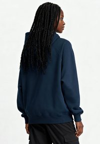 Sweat à capuche bleu marine en tissu mélangé coton, doté d'une capuche spacieuse, de poignets côtelés et de coutures latérales, porté avec un pantalon cargo noir.