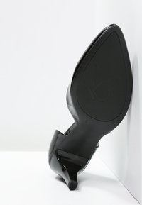 Chaussure à talon haut en cuir verni noir avec un bout pointu et un talon fin. La semelle texturée présente un logo de papillon.